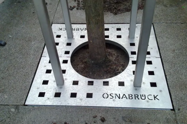 Baumschutzgitter mit Logo Schriftzug und nivellierbaren Stelen mit Sollbruchstelle